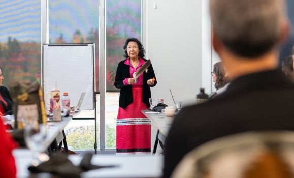 Elder Ann LaBillois is standing at the front of a classroom holding a feather.