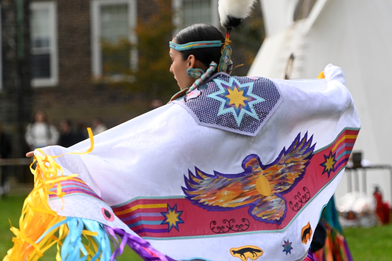 Dancer with arms outspread wearing traditional clothing featuring eagle and star icons.