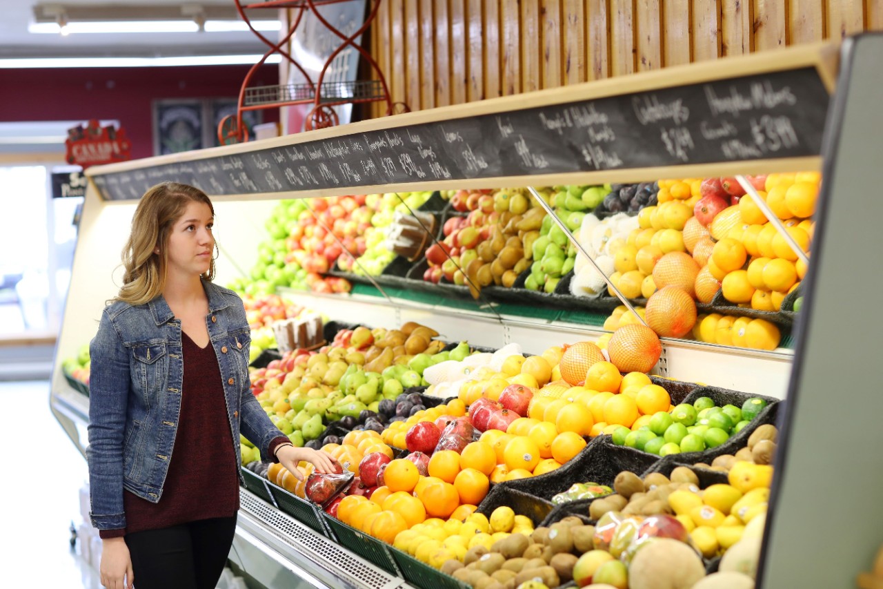 A woman looks at prices of fruit in a grocery isle. 