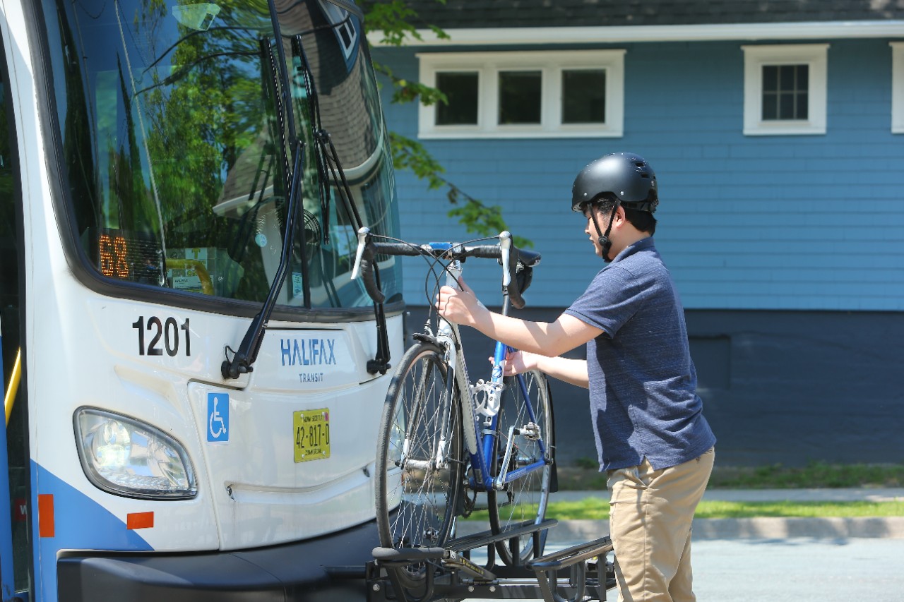 A cyclist wearing a helmet affixes his bike to a rack at the front of a Halifax Transit bus.