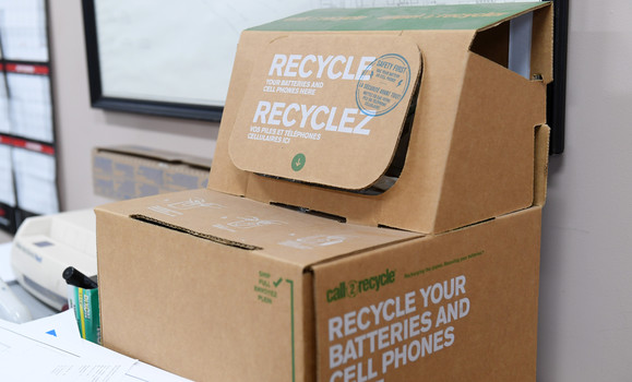 A cardboard recycle bin with the text' Recycle your batteries and cell phones'. 