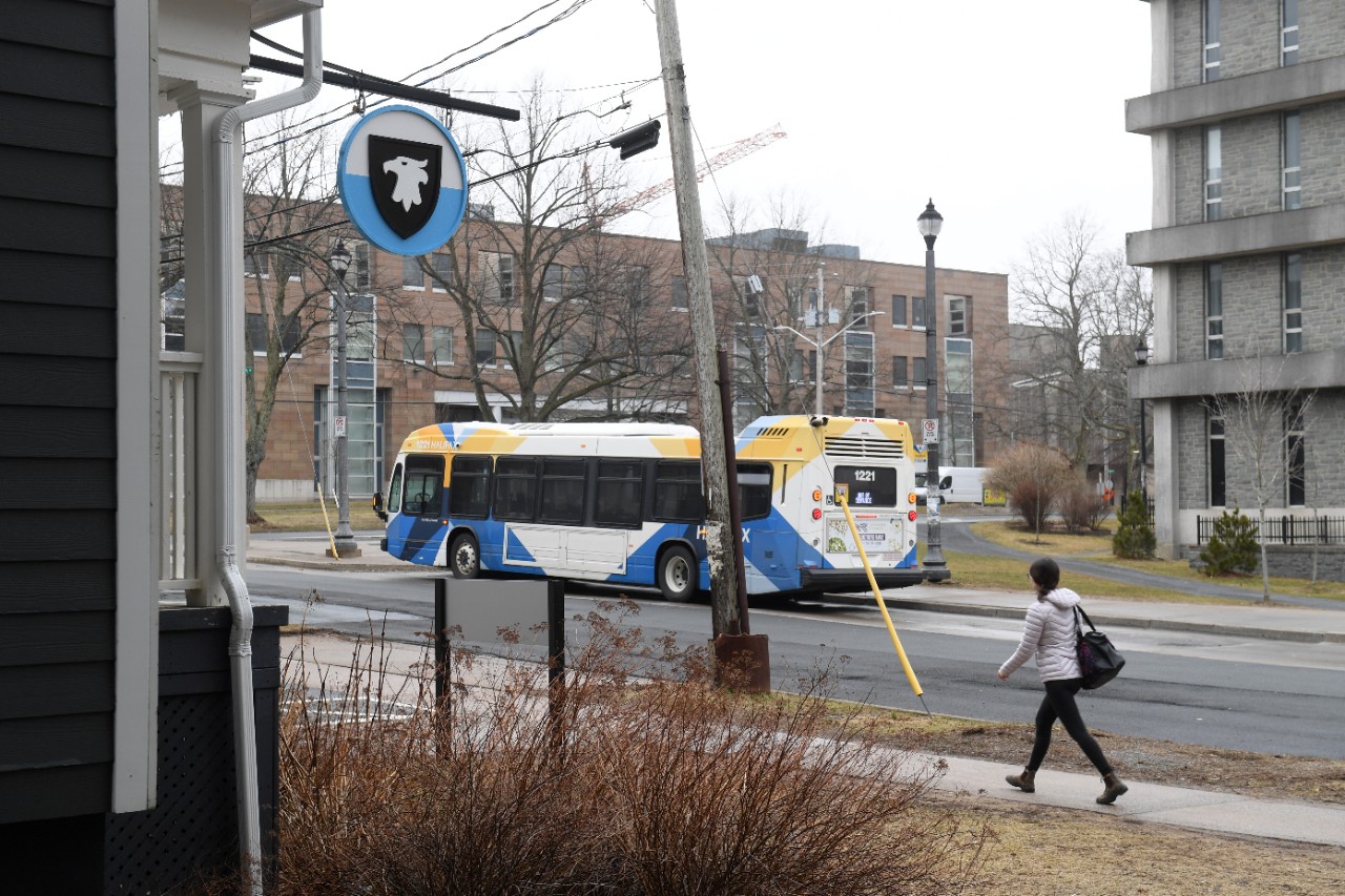 A student walks on the sidewalk across the street from a bus is parked at a bus stop next to Dal's SUB.