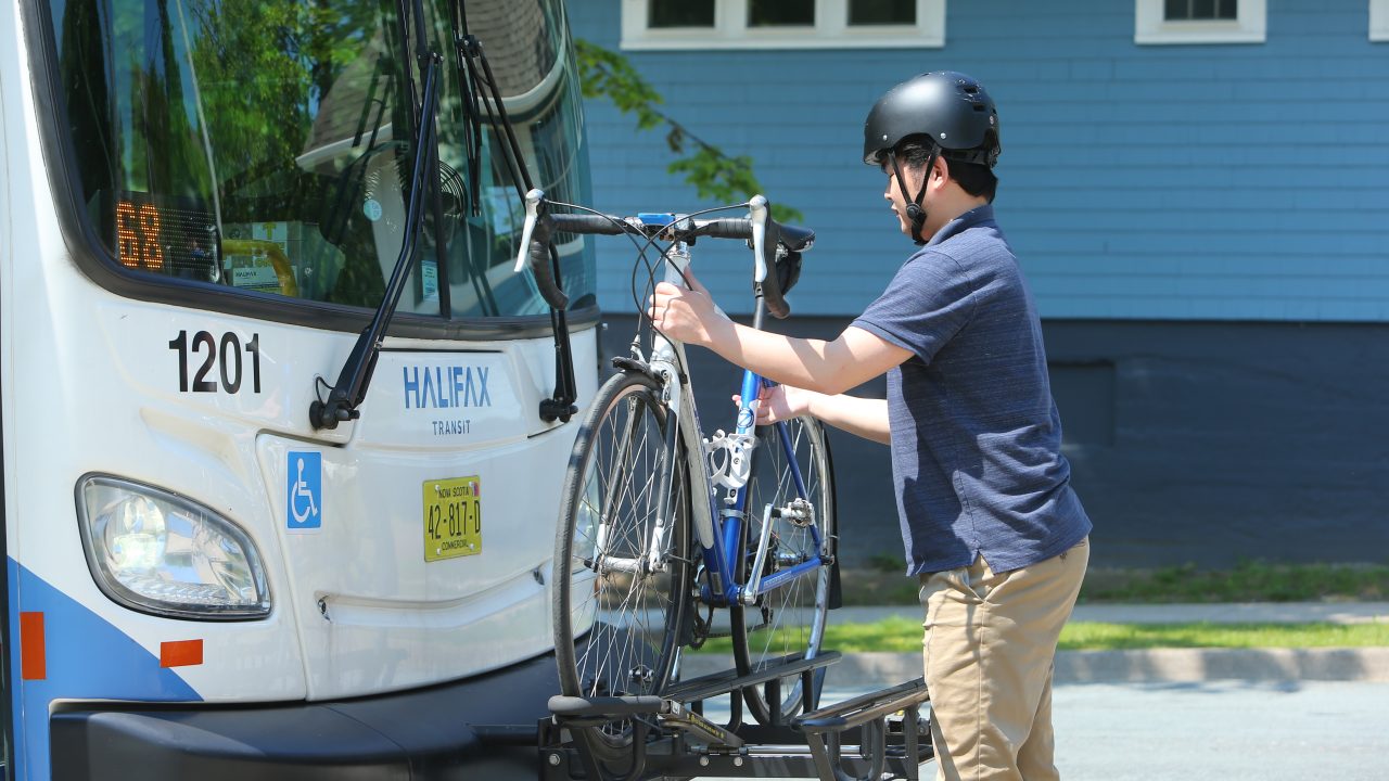 A cyclist wearing a helmet affixes his bike to a rack at the front of a Halifax Transit bus.