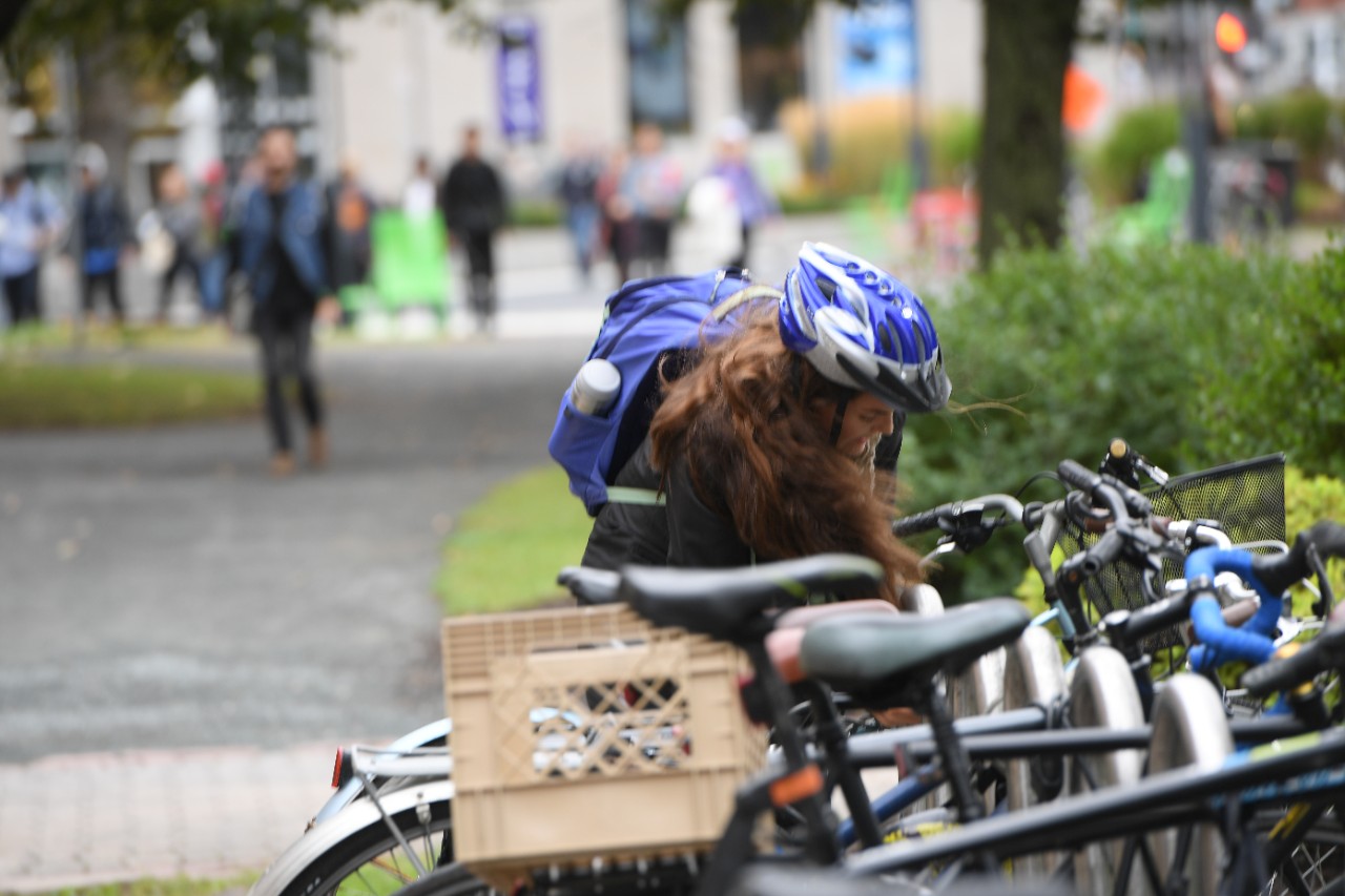 A student wearing a blue backpack and helmet unlocks her bike from a full bike stand.