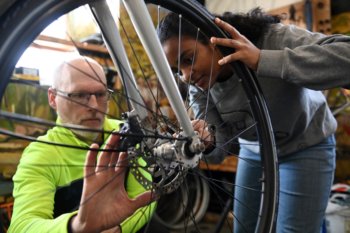 A Bike Centre employee and a student kneel over a bike wheel to adjust gears.
