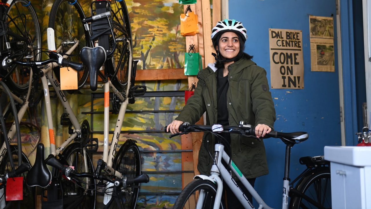 A student wearing a helmet smiles next to a white bicycle outside the Dal Bike Centre.