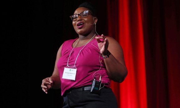Masters of Marine Management student Kristal Ambrose speaks on a stage with red curtains.