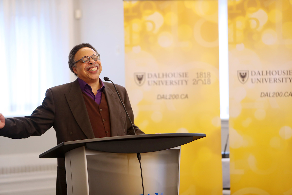 George Elliott Clarke recites the Bicentennial Poem while standing at a podium in front of a gold Dalhousie sign. 
