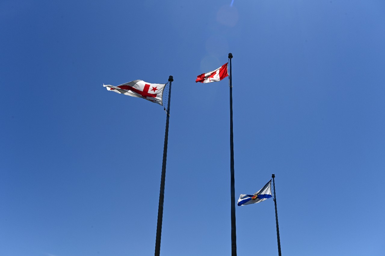 Three flags on flagpoles with a clear blue sky.