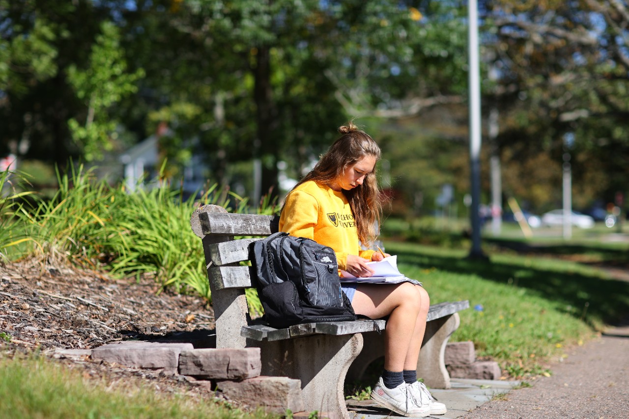 Student studies on bench outside.