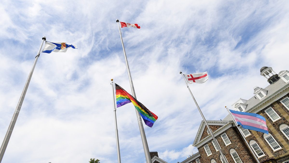 The Nova Scotia, Canadian, Mi'kmaq, pride, and trans flags flying on the Studley Quad. The MacDonald Building can be viewed in the backgroudn.
