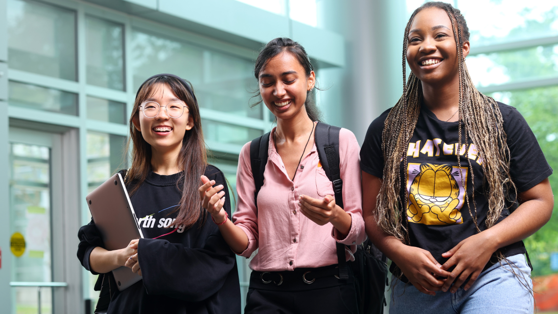 Three students chat as they walk through the lobby of the Rowe Management Building.