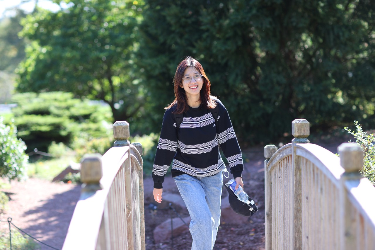 Student walking on wooden footbridge smiling.