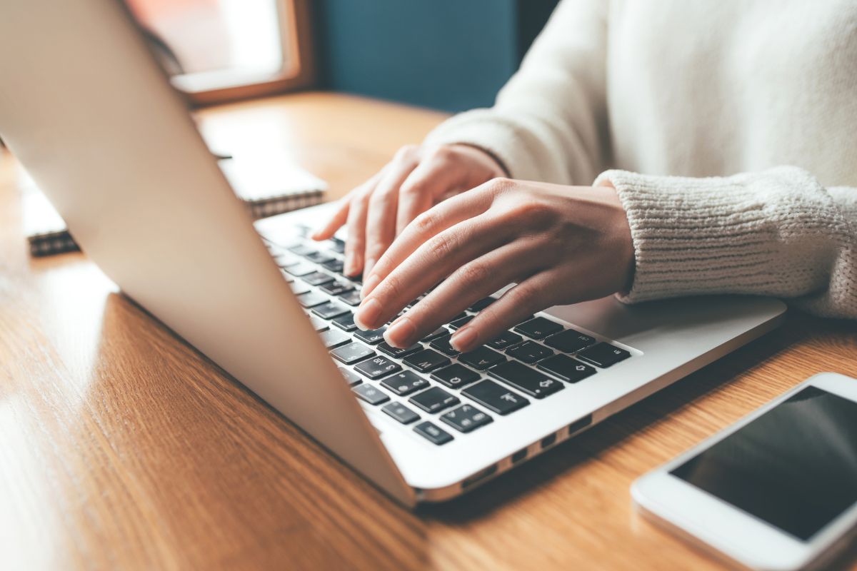 A person's hands are shown typing on a laptop atop a desk.
