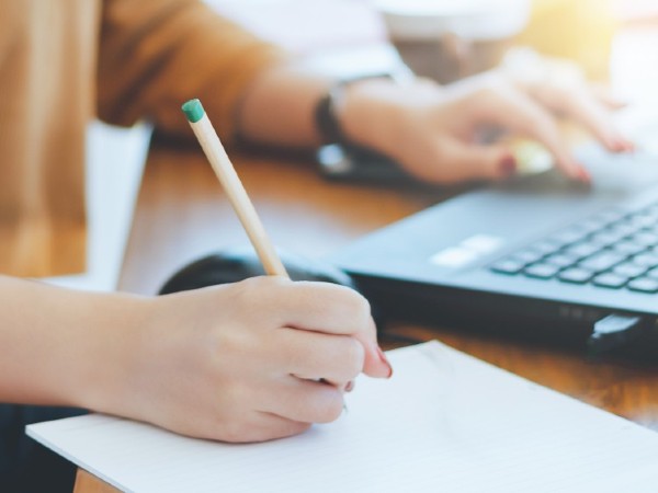 One hand writing on a piece of paper, and one hand typing on a laptop.