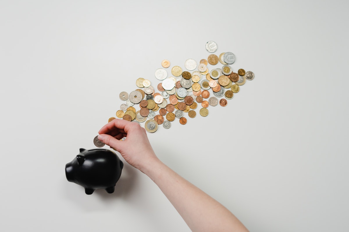 A hand places a coin in a black piggybank with assorted coins beside it.