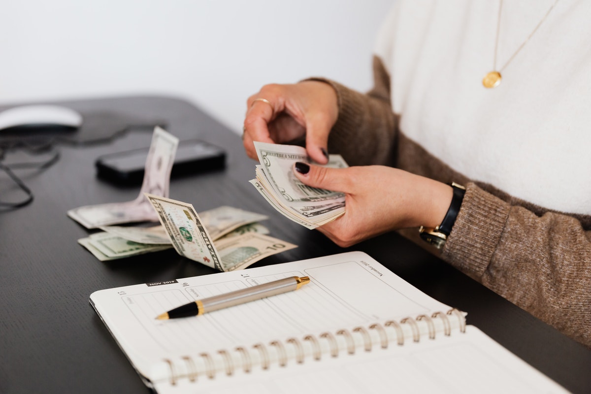A person counts out money on a table with a notebook and pen sitting in front.