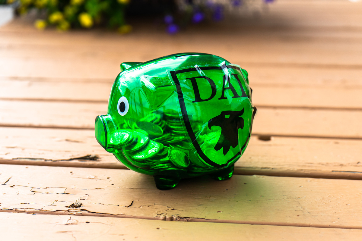 A green piggy bank with a Dal logo on it sits on a wooden floor.