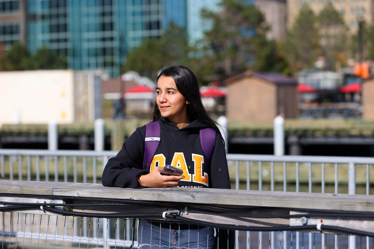 A student leans on wharf railing with buildings on the Halifax Waterfront in the background.