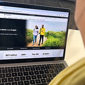 Looking over the shoulder of a student who is looking at a computer displaying the new Dal.ca homepage.
