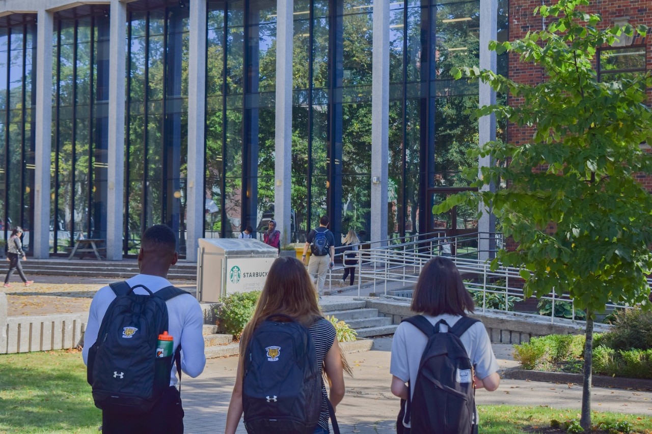 Three students with backpacks walking to the glass-fronted Tupper Link building.
