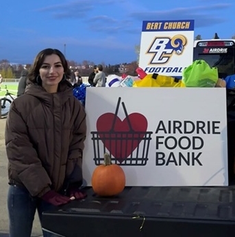 Portrait of Reese Ochitwa standing beside a sign that says Airdrie Food Bank.