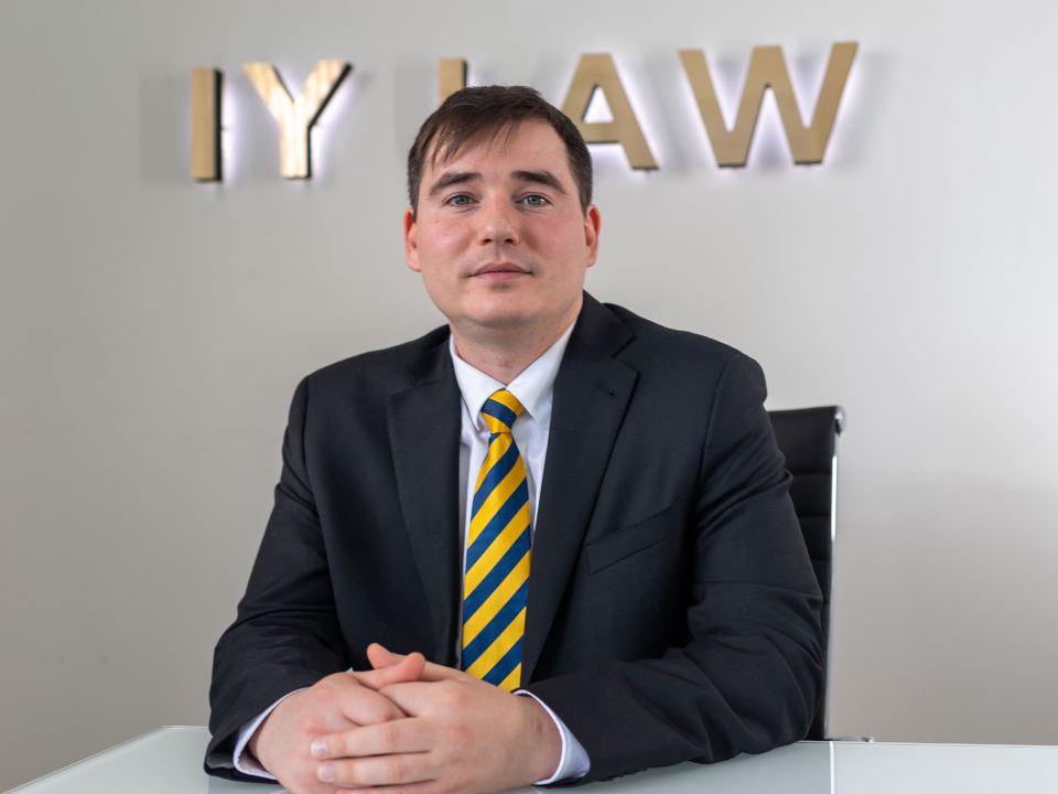Arum Award Winner Igor Yushchenko sitting at desk in front of IY Law firm logo.
