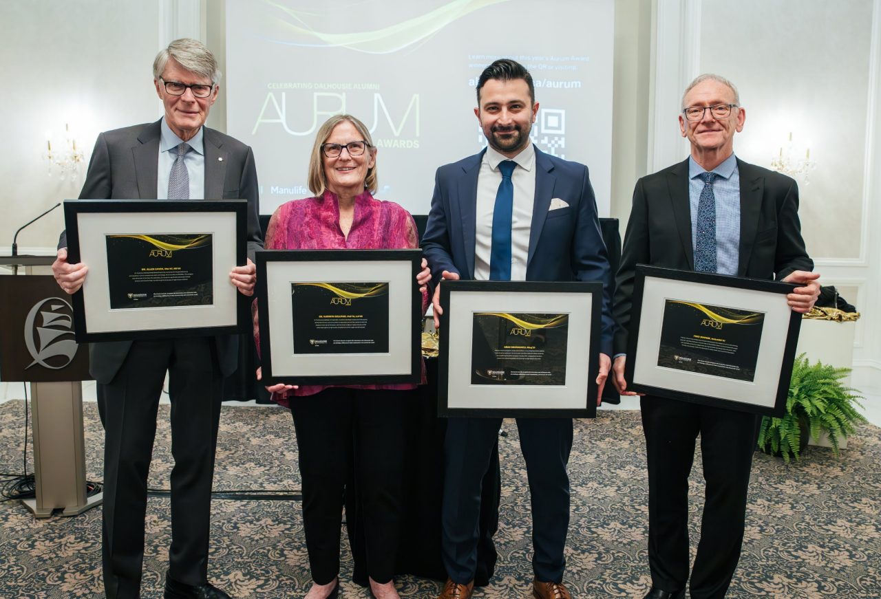 The award recipients stand together displaying their framed award certificates dressed up for the event.