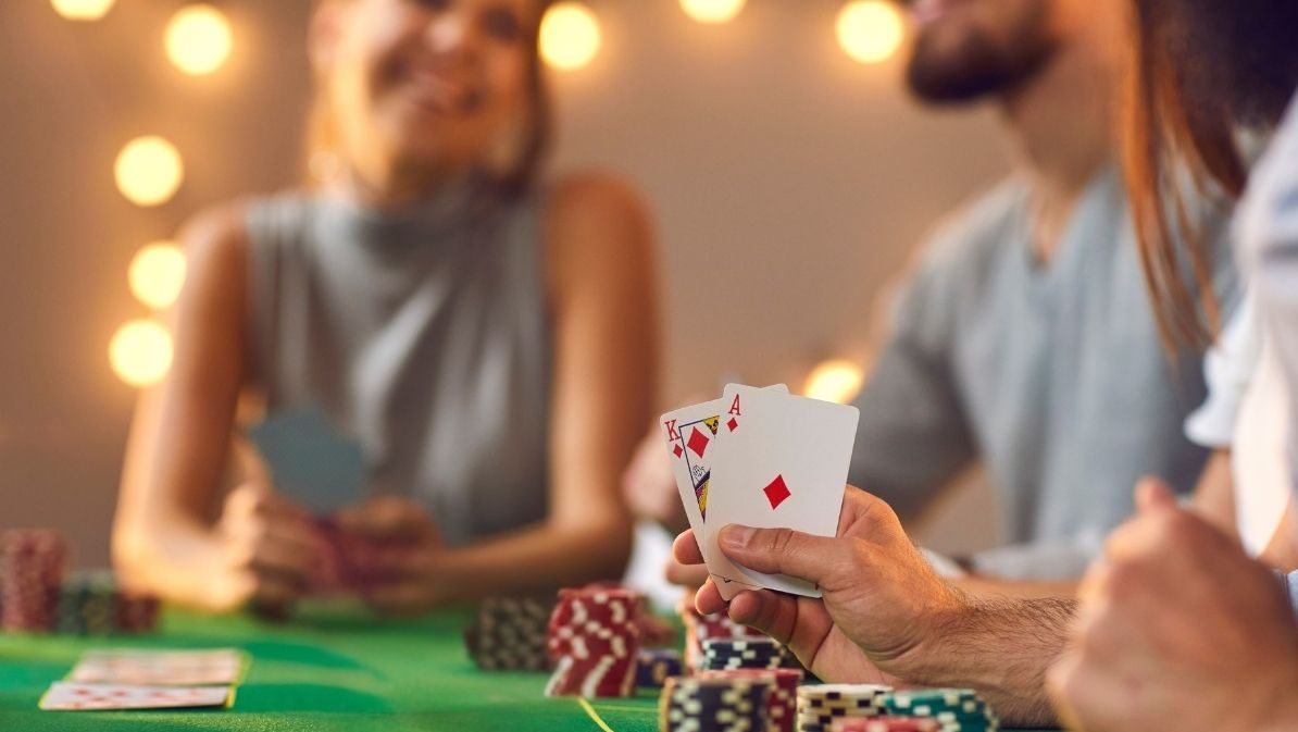 Several people playing a card game with casino chips under twinkly lights.