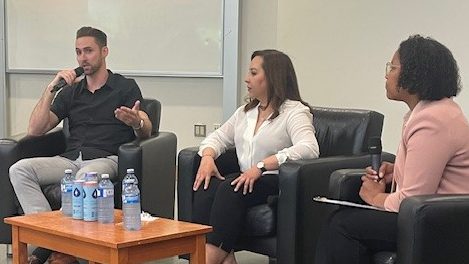 Three alumni panelists are sitting in chairs talking at an event.