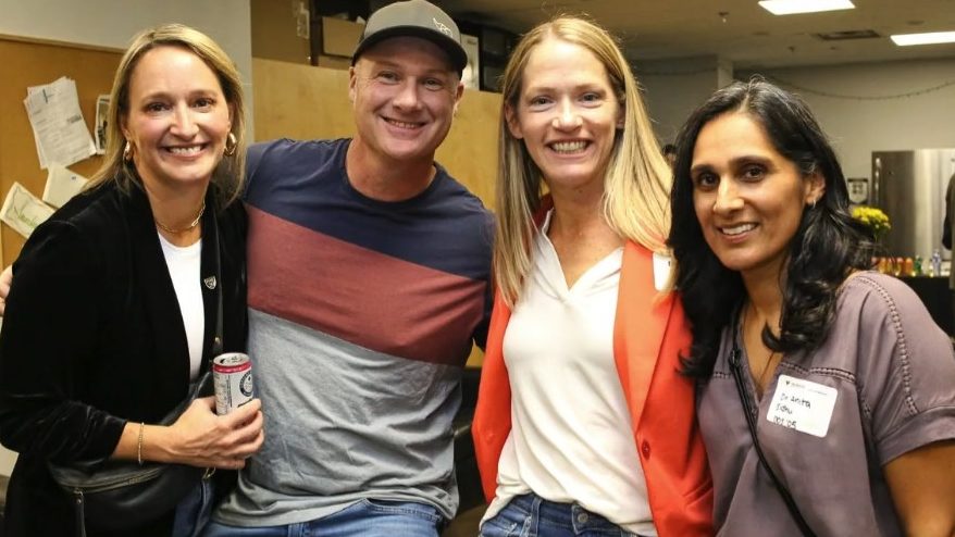 Four alumni standing together at a casual event.