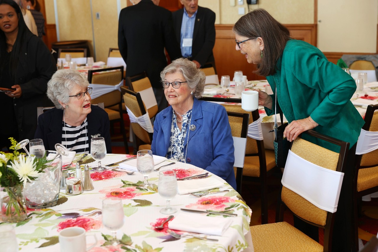 Alumni of all ages seated and standing while mingling at the spring breakfast event.