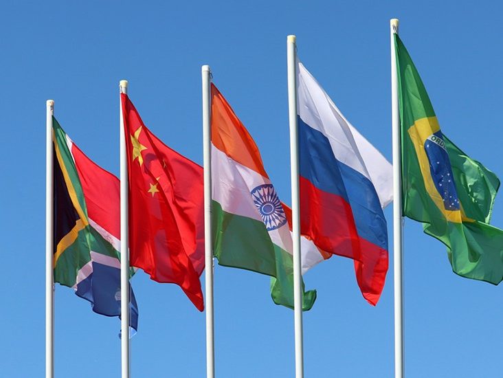 The flags of the countries originally associated with BRICS on flag poles against blue sky.