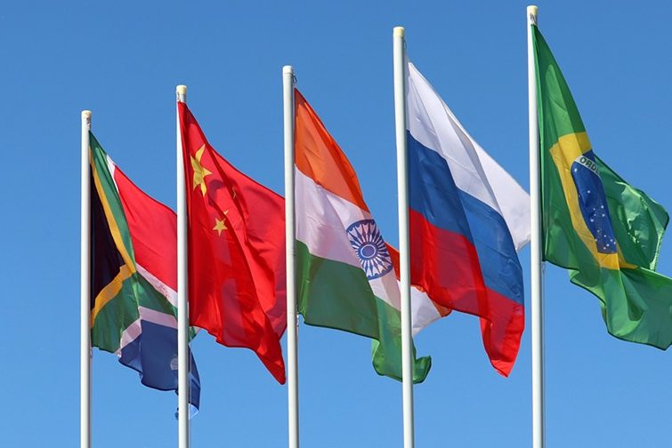 The flags of the countries originally associated with BRICS on flag poles against blue sky.