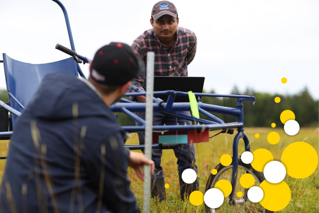 Two people in a field with a piece of agriculture equipment.