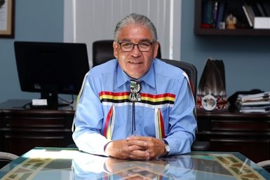 Chief Sidney Peters sits at a table in his office with his hands clasped and smiling.