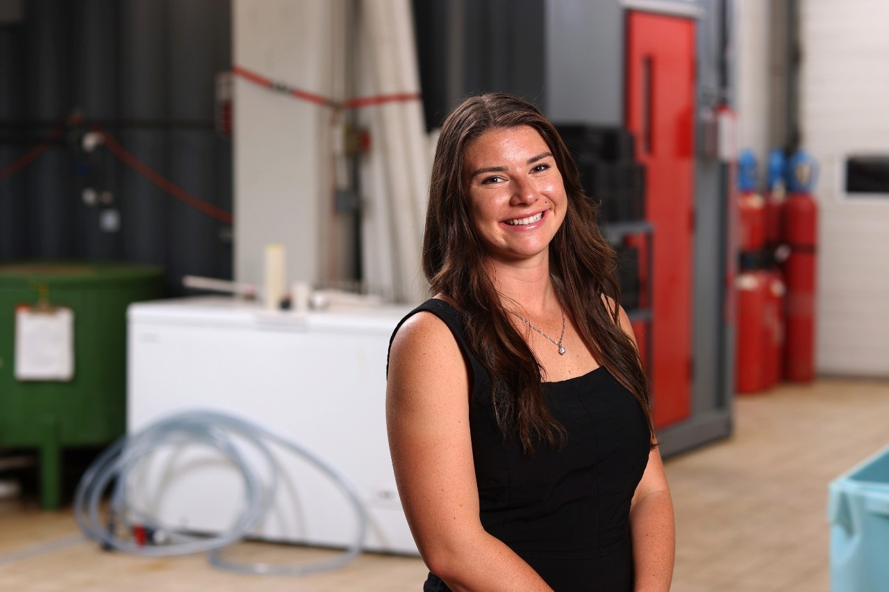 A woman with long brown hair smiling in business casual attire while in a food processing plant.