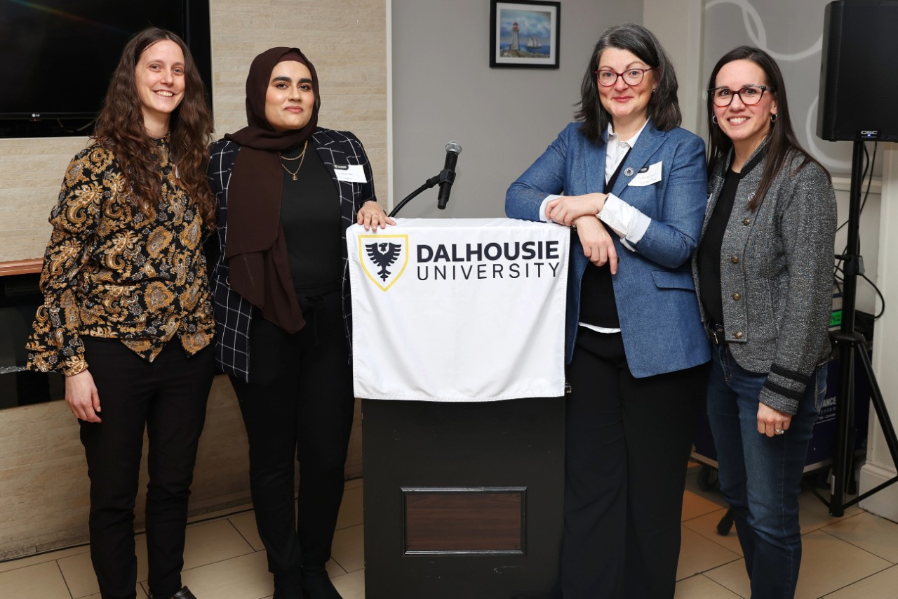 The three women in STEM event speakers and the host standing in front of the podium.