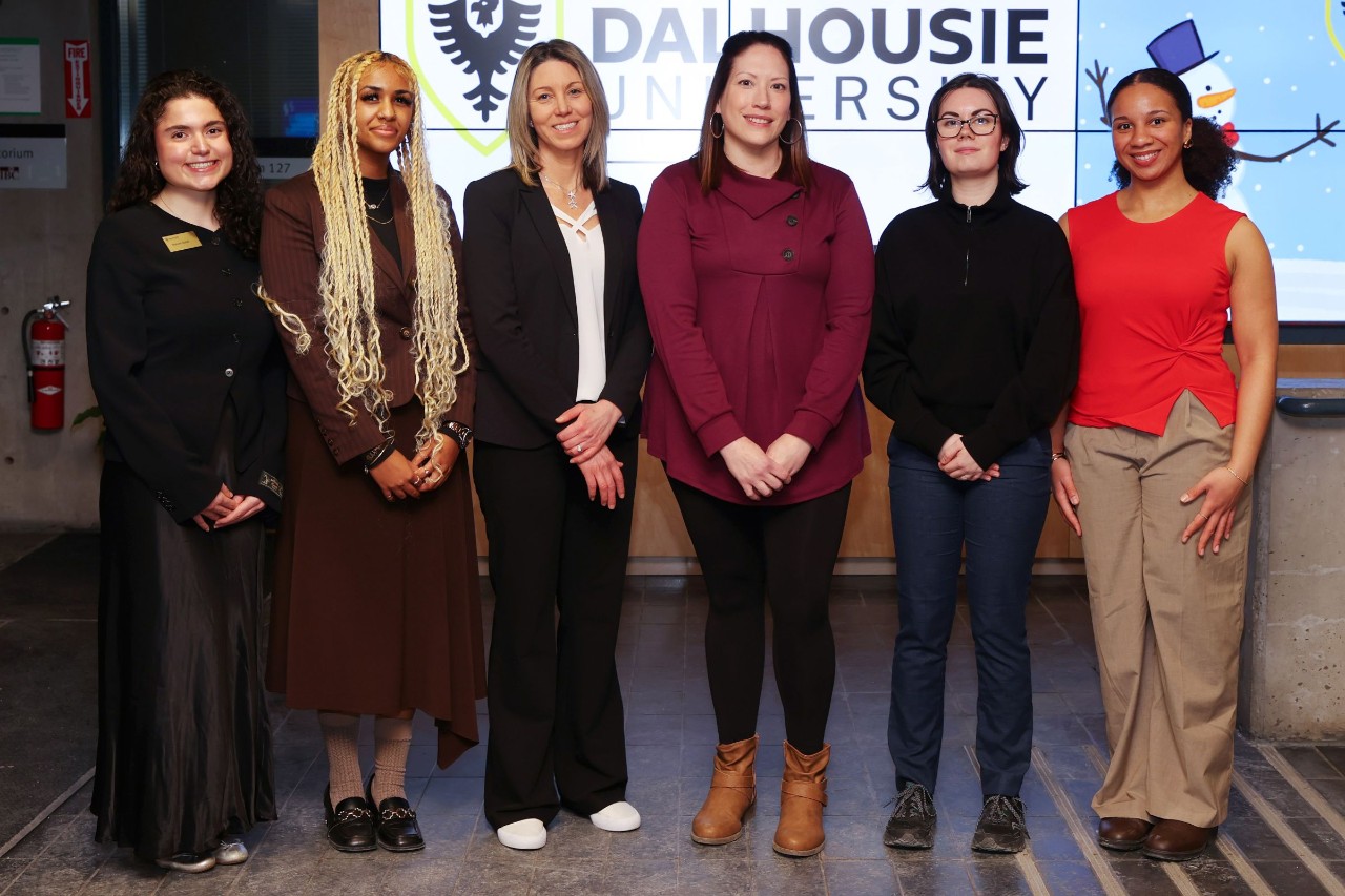 Six women stand together smiling at an indoor event.