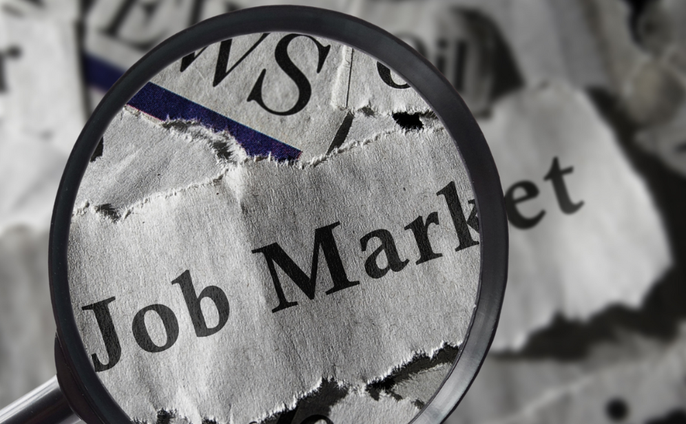 A magnifying glass over newspaper clippings of headlines is focused on the words, “Job Market.”