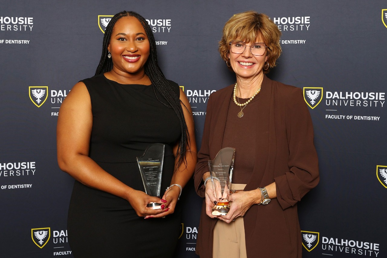 Two women stand together holding awards at a semi-formal event.