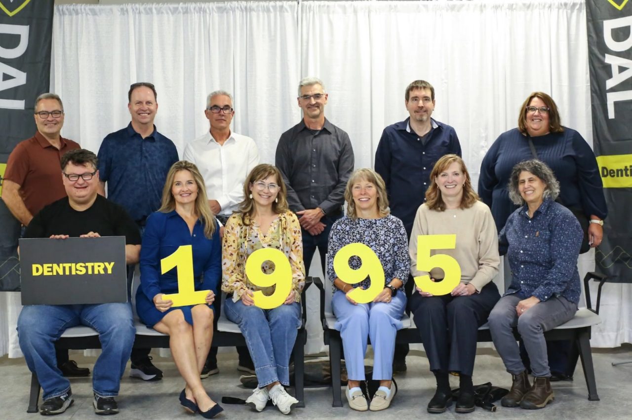 A group of twelve people with the back row standing and front row seated at a casual reunion event for "1995."