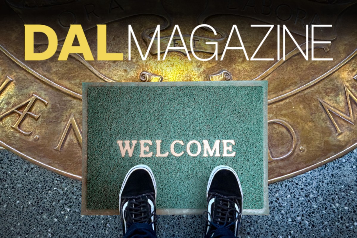A person's feet in black and white sneakers stand on a green welcome mat atop the Dalhousie University Coat of Arms engraved on the lobby floor. 