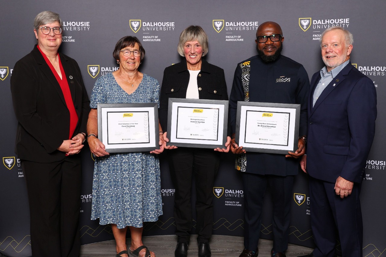 Five people standing together at an event with three holding framed certificates.