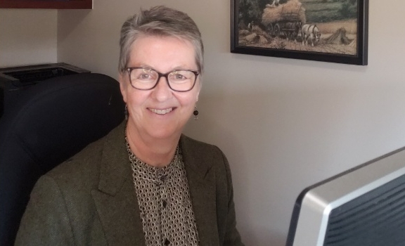 Ronda Bellefontaine smiling wearing glasses, looking up from her computer in an office space.