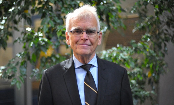Robbie MacKeigan in suit and tie with greenery in the background.