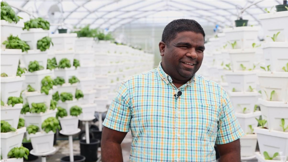 Mullaivannan Manoharan standing in a greenhouse with stacks of plants in white pots.