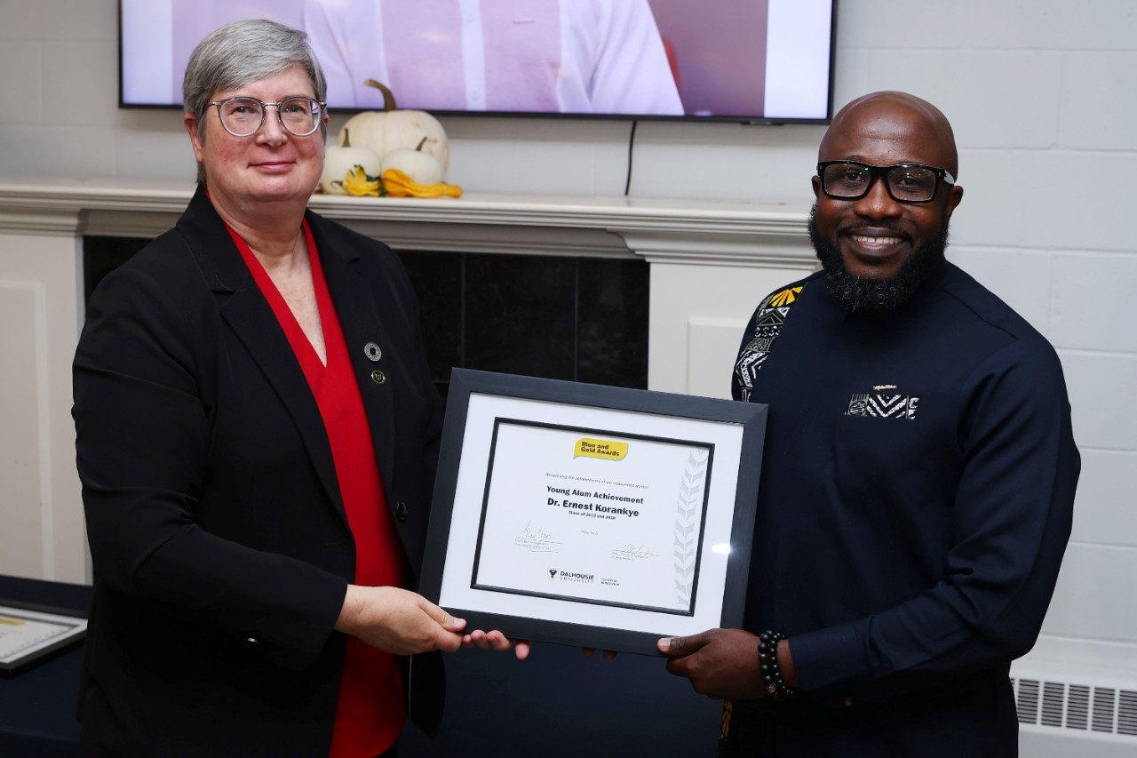 A women and a man smiling at an event holding a framed certificate between them.