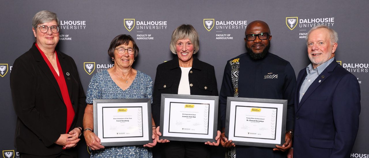 Five people standing together at an event with three holding framed certificates.