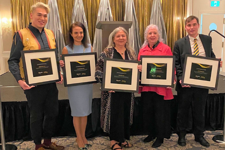 Five people pose with framed certificates at an event.